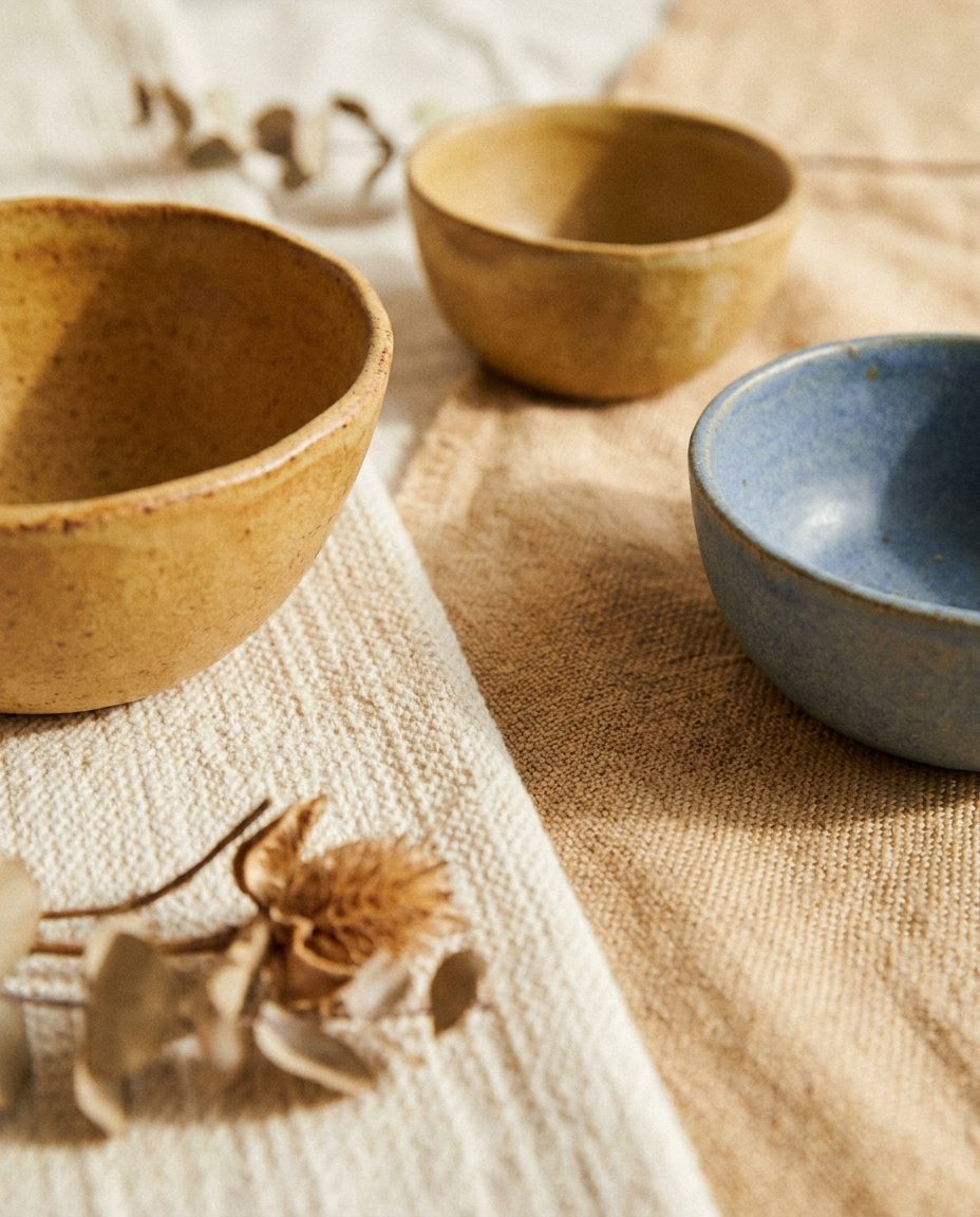 A close still life of handmade wooden and ceramic bowls on a warm wooden surface, soft daylight, one dusty blue bowl among warm tans.